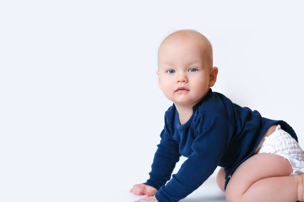 istock Baby in blue shirt and diaper with copyspace for text crawls on the floor overwhite studio background. little caucasian child looking at camera 1224431679