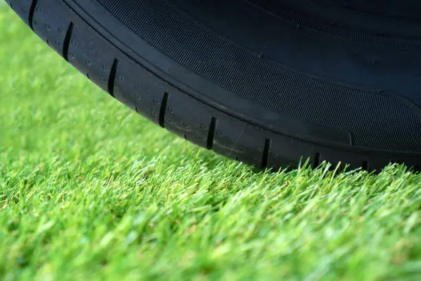 Durable artificial grass lawn concept with wheel tire on the green synthetic turf.