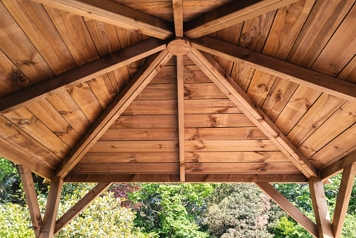 The inside roof of a wooden garden gazebo, looking up and out from within.
