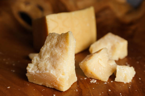 Pieces of parmesan or parmigiano reggiano cheese on a wooden board. Pieces of parmesan or parmigiano reggiano cheese on a wooden board. Parmesan cheese uses in pasta, risotto and salads. Close-up. grana padano stock pictures, royalty-free photos & images