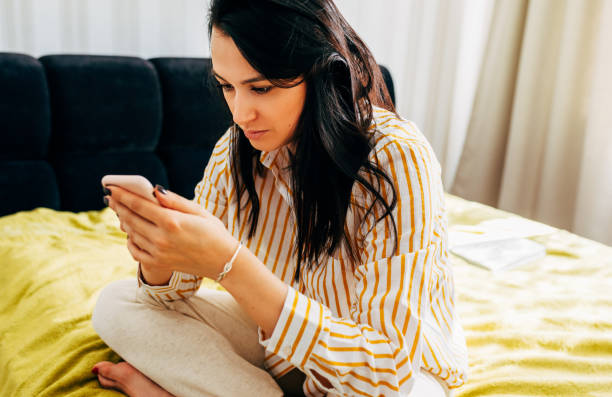 istock Brunette young woman using mobile phone while working at home. Female freelance wearing striped shirt messaging with smartphone. Beautiful stylish lady browsing site on cellphone. 1224437067