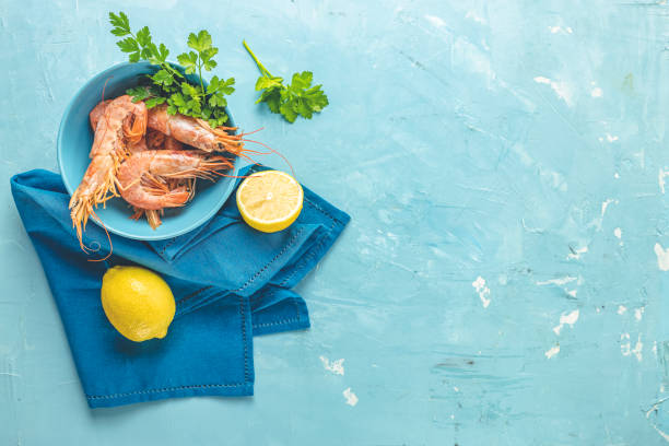 Shrimp, prawn with parsley in blue ceramic plate surrounded napkin and lemon on light classic blue concrete table surface. Healthy seafood background with copy space for you text. stock photo
