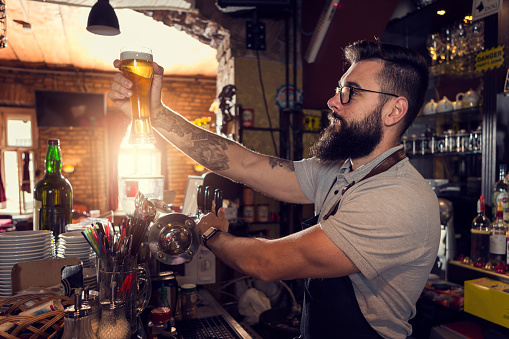 Bearded Bartender pouring beer from beer tap in a bar
