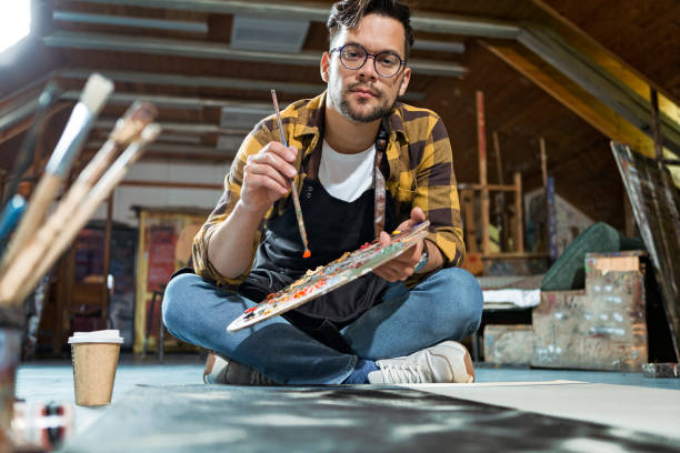 istock Artist in a studio sitting on a floor painting 1224442837