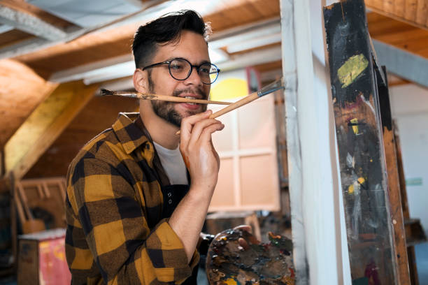 istock Male painter at art studio indoors painting holding brush between his teeth 1224442924