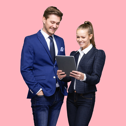 Front view of aged 20-29 years old who is beautiful caucasian young male businesswoman standing in front of colored background wearing blazer who is happy and using digital tablet