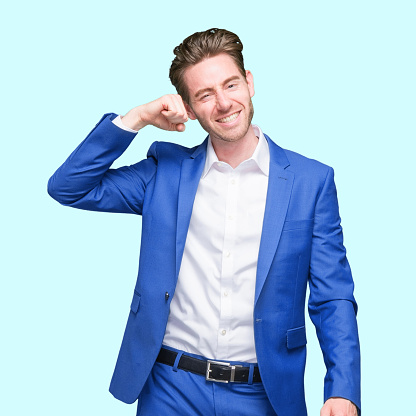 Waist up of with short hair caucasian young male businessman dancing in front of blue background wearing businesswear who is excited and cheering and showing fist who is and doing fist pump