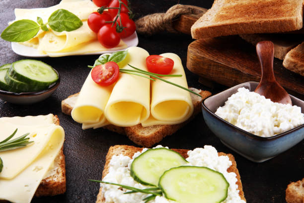 rolled slices of golden gouda cheese or cream cheese on a sandwich garnished with sliced cucumber and herbs. bread or toast with cheese for breakfast