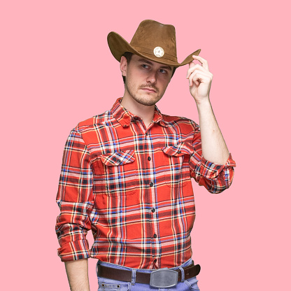 Portrait of aged 20-29 years old with short hair caucasian young male cowboy standing in front of colored background wearing lumberjack shirt who is in concentration