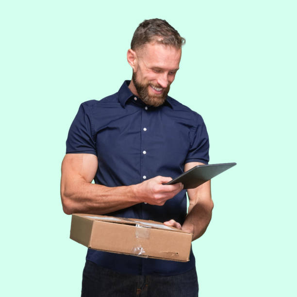 istock Caucasian young male manual worker standing and holding cardboard box and using touch screen 1224459595