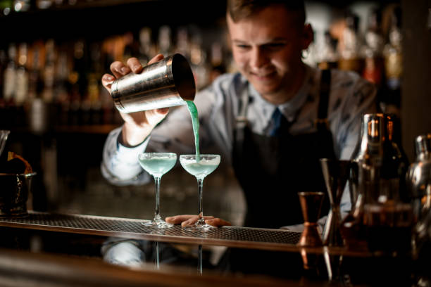 istock Smiling young barman pours ready-made cocktail from shaker into glass. 1224461627