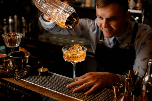 istock Young smiling bartender pours finished cold cocktail from glassy shaker into glass. 1224463240