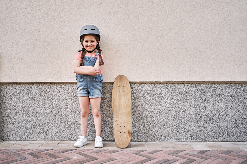 Adorable excited 5 years old girl learning longboarding at the front yard while wearing protective helmet