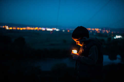 Cute boy standing near river with candle at night