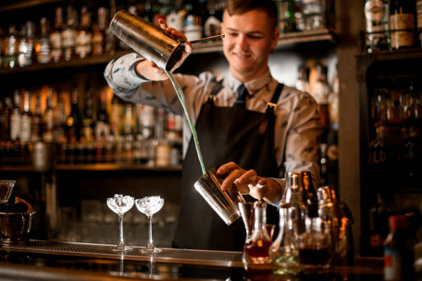 istock Young smiling barman pours cocktail in shaker. 1224465388