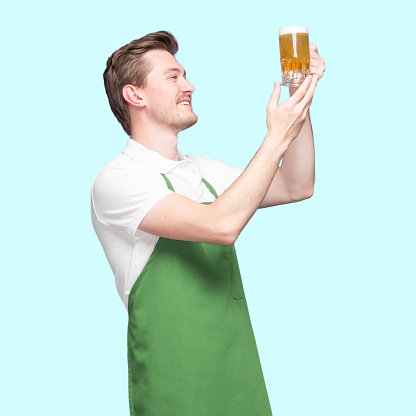 Inspector / inspect / -  one person of with short hair caucasian young male standing in front of blue background wearing polo shirt who is looking who is examining and holding pint glass