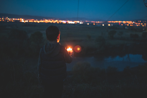 Cute boy standing near river with candle at night