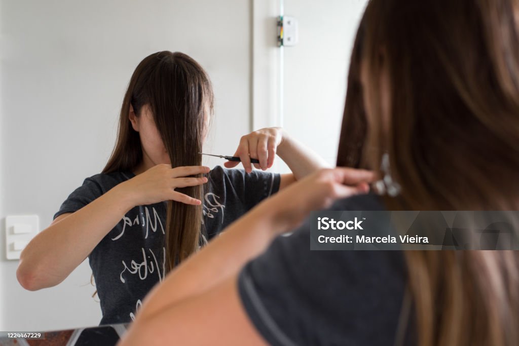 Woman cutting her own bangs Woman with long brown hair cutting her own bangs Cutting Stock Photo