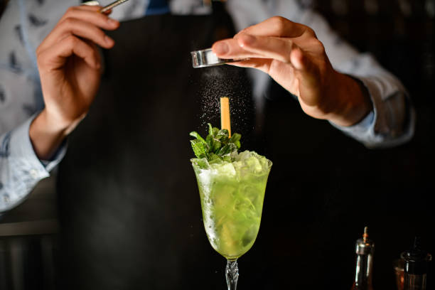 istock barman decorates by powder ready-made cocktail with two sticks and mint leaves 1224468054
