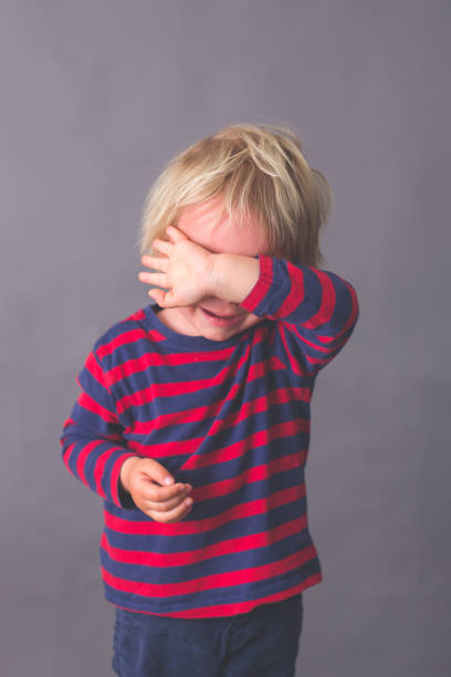 Little toddler child, boy, crying, hiding his face with hand, isolated image on gray Little toddler child, boy, crying, hiding his face with hand, isolated image on gray background child laughing hysterically stock pictures, royalty-free photos & images