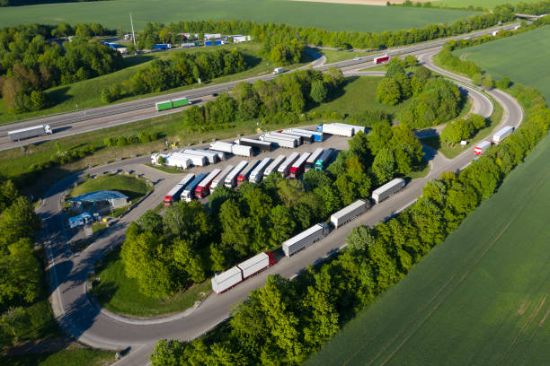 Heavy goods transportation - trucks in truck stop from above. Rush hour on the highway is seen in the background.