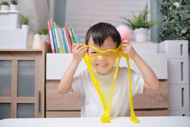 азиатский детский сад школьник весело сделать желтый пушистый слизь, молодой ребенок весело играть и быть творческим по науке эксперимент  - kid made стоковые фото и изображения