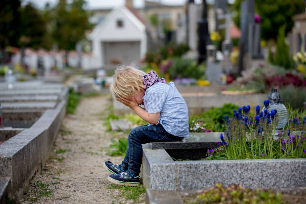 mały maluch, siedzący na grobie na cmentarzu, smutny i samotny, wiosną - cemetery child mourner death zdjęcia i obrazy z banku zdjęć