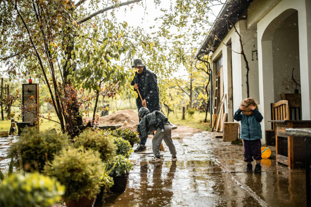figlio che aiuta il padre e spazza l'acqua dal cortile nella giornata piovosa - alluvione foto e immagini stock