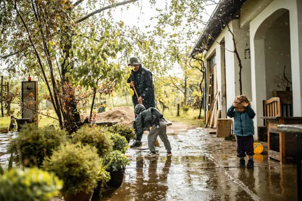 Photo of Son helping father and sweeping water from front yard on rainy day