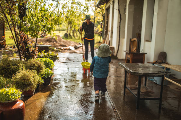 istock Young woman sweeping water from front yard on rainy day 1224471725