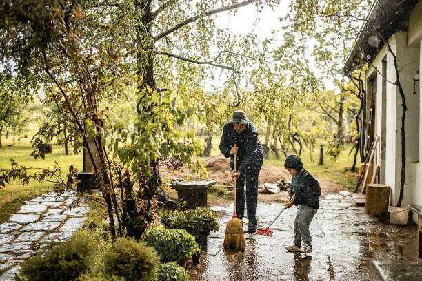 Father and son sweeping water from front yard on rainy day Father and son sweeping water from front yard on rainy day broom photos stock pictures, royalty-free photos & images