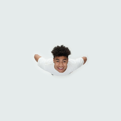 Aerial view of aged 18-19 years old with curly hair african-american ethnicity male standing in front of white background wearing shirt who is excited with hand on hip