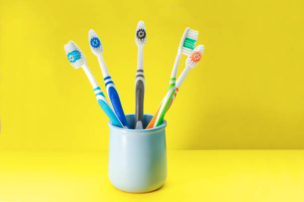 istock Multicolored toothbrushes in a blue glass on a yellow background. Close up. 1224477260