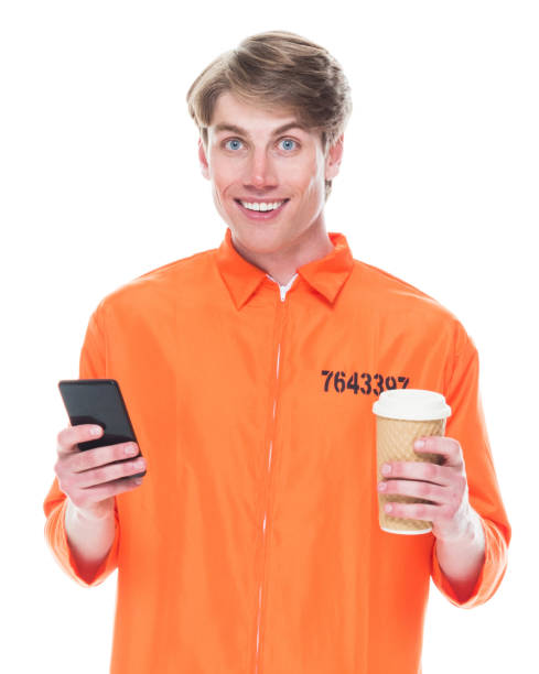 caucasian male criminal in front of white background wearing jumpsuit and holding coffee cup and using mobile phone - prison cell imagens e fotografias de stock