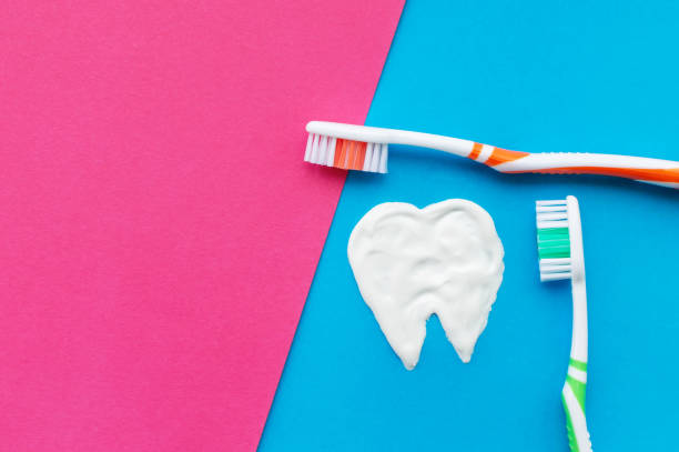 istock Multi-colored toothbrushes on a blue and pink background with a tooth pattern drawn with toothpaste. The view from the top. 1224479336