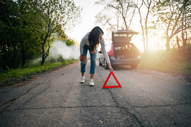 Oh no, my car broke down in the middle of nowhere! Young and beautiful woman placing the warning triangle symbol in front of her broken down car. She looks worried and sad because she is away from city and it is getting dark tow truck stock pictures, royalty-free photos & images