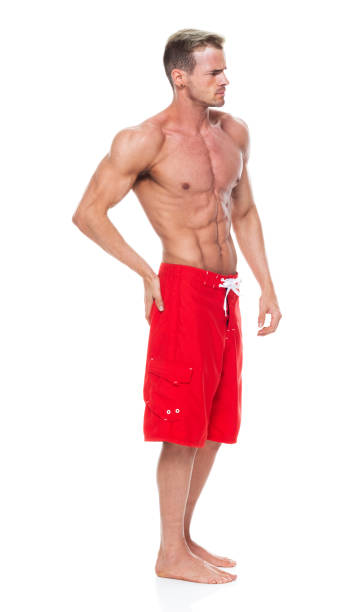 kaukasier junge männliche rettungsschwimmer vor weißem hintergrund tragen board shorts und aktiv mit bodybuilding - body building men flexing muscles male stock-fotos und bilder
