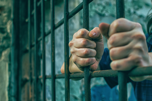 A depressed man in handcuffs behind bars. A depressed arrested male offender is jailed. Shouts, breaks, cries.