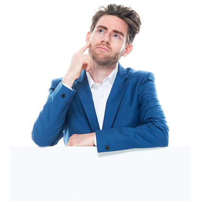 Front view of aged 30-39 years old with brown hair caucasian young male businessman standing in front of white background wearing jacket who is asking who is showing with hand and holding sign with copy space