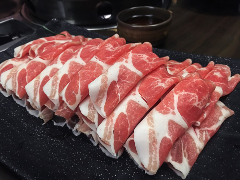 Close up shot of collection thin beef slices for hot pot, placed above a plate in a restaurant