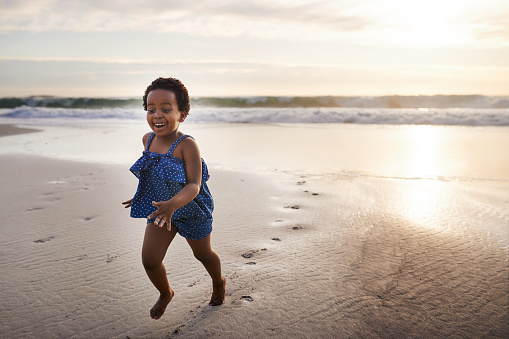 Shot of an adorable little girl having fun on the beach at sunset