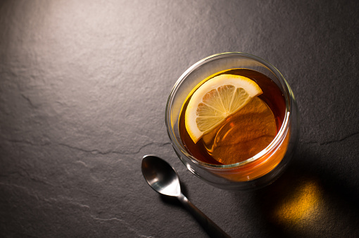 Top view image of a cup of tea with lemon on a black granite background