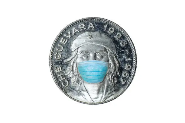 Che silver coin with surgical mask on Che Guevara from Cuban revolutiuon. Concept and symbol of Cuba island in Covid-19 time. SARS-CoV-2 pandemic and Cuban Coronavirus quarantine. White background.