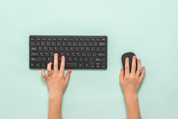 istock Hands of a child with a black keyboard and mouse on a light background. 1224496948