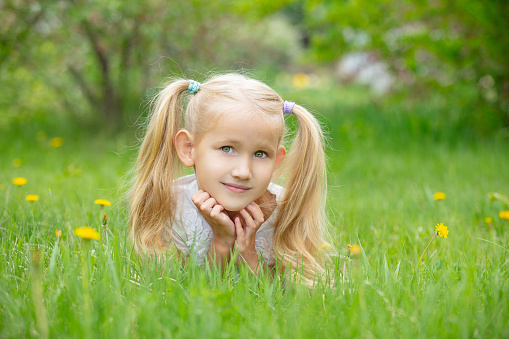 A 6 year old girl with blond hair  is crouching within the grass and flowers of a country field. Photo taken on Lemnos island in Greece.