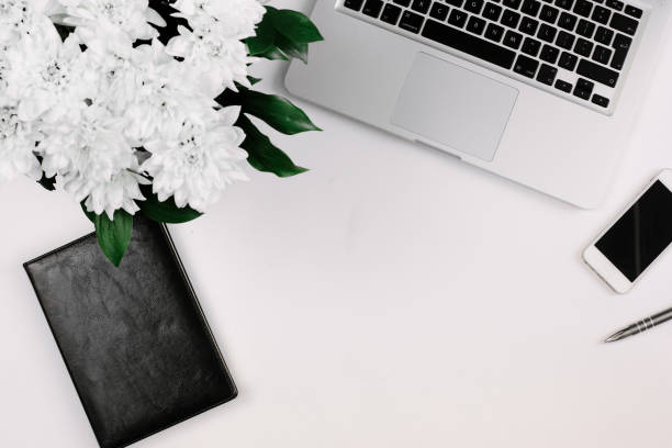 istock Workspace with laptop, notebook, smartphone, pen and flowers bouquet on white table. Flat lay, top view 1224506756