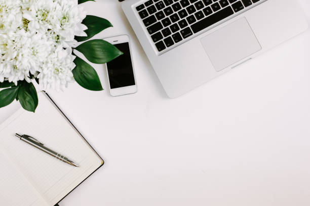 istock Workspace with laptop, notebook, smartphone, pen and flowers bouquet on white table. Flat lay, top view 1224506789