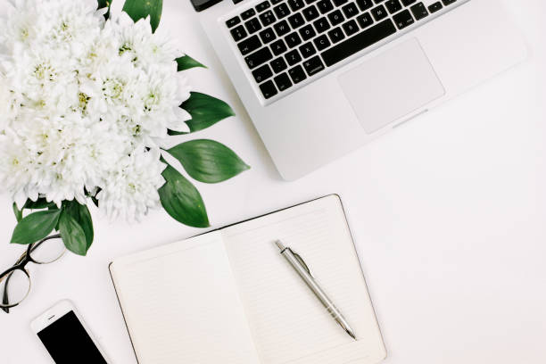 istock Workspace with laptop, notebook, smartphone, pen and flowers bouquet on white table. Flat lay, top view 1224506809