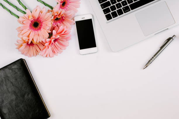 istock Workspace with laptop, notebook, smartphone, pen and flowers bouquet on white table. Flat lay, top view 1224506822