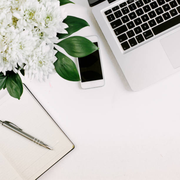 istock Workspace with laptop, notebook, smartphone, pen and flowers bouquet on white table. Flat lay, top view 1224506844